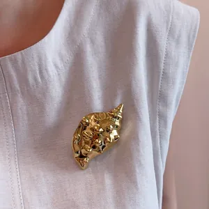 Macro detail of high-polish 18K gold-plated conch shell brooch on linen fabric