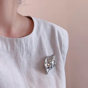 Detail of silver conch shell brooch with mirror finish pinned on beige linen garment