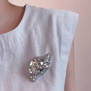 Detailed close-up of a metallic conch brooch with silver finish pinned on a grey vest