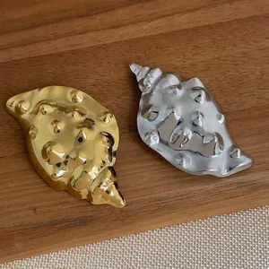 Detail of conch brooches in 18K gold and silver plating on a wooden display