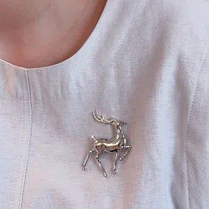 Macro shot of polished silver elk brooch on light grey linen fabric texture detail