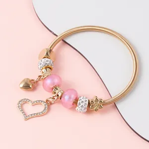Detail of gold spring charm bracelet featuring pink beads and heart rhinestone pendants