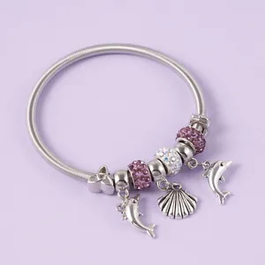 Macro shot of silver charm bracelet featuring crystal dolphin and seashell pendants