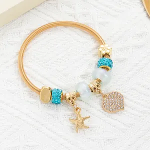 Close-up of golden spring bracelet with starfish and pavé heart charms on lace background