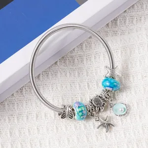 Detail of silver alloy bracelet with starfish, turtle, and shell charms on white fabric