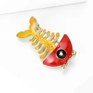 Detail of creative fishbone brooch with red enamel head and golden metal skeleton finish