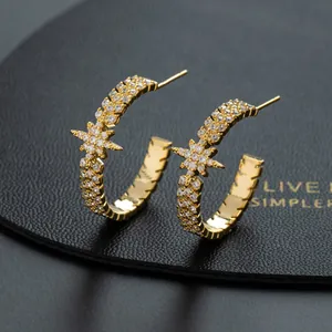 Detail view of gold C-shaped earrings with clear zircon stones and star motif
