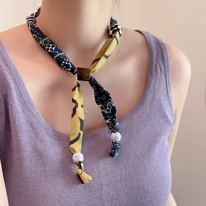Detail van zijden sjaalketting met paisley-print, marmeren kralen en dambord-bedeltje