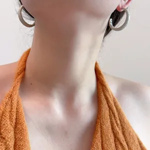 Gros plan d'une femme portant des boucles d'oreilles créoles beige à texture cuir