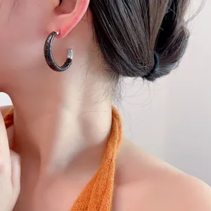Gros plan de boucles d'oreilles créoles en cuir noir avec détails argentés sur un modèle