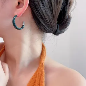 Détail de boucles d'oreilles créoles en cuir crocodile vert foncé portées par un mannequin