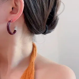 Gros plan d'une femme portant des boucles d'oreilles en C avec cuir bordeaux façon crocodile
