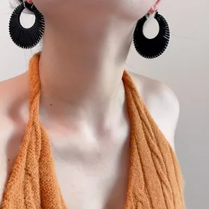 Détail de grandes créoles noires texturées portées par un mannequin sur fond neutre uni