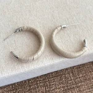 Détail de boucles d'oreilles en C argentées avec cuir beige texturé serpent et fini poli