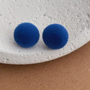 Close-up of blue flocked ball stud earrings on a textured stone tray with soft lighting