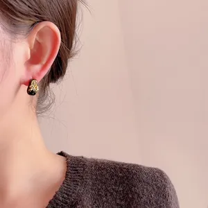 Elegante gouden strik oorbellen met zwart email en kristal op een vrouwelijk oor