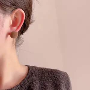 Close-up of brown flocked round stud earring on model with autumn knitwear style