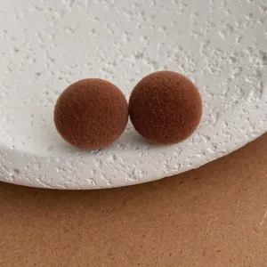 Close-up of brown flocked sphere earrings on textured white and craft paper background