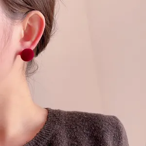 Macro shot of a deep red velvet round stud earring worn on a model earlobe