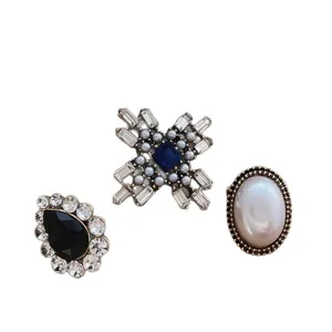 Set of three vintage-style brooches with blue crystals, black gems, and pearls on white background