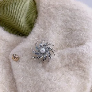 Detailed view of silver fireworks swirl brooch with pearl on a white textured coat lapel