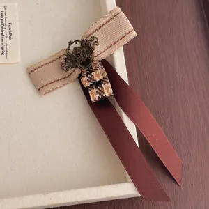 Detail of vintage beige woven ribbon and long dark red silk bow with antique floral brooch