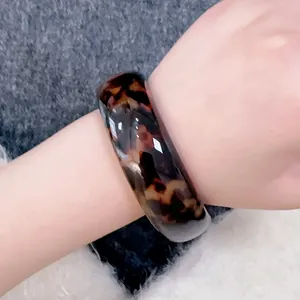 Close-up of a wide resin leopard print bangle with tortoiseshell pattern on wrist