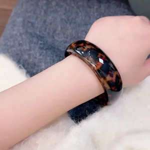 Close-up of wide leopard print resin bangle on wrist with vintage tortoiseshell texture
