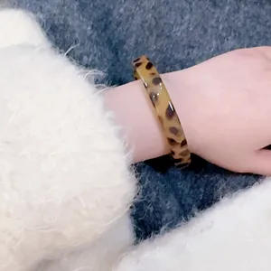 Fashionable leopard print resin wide bangle bracelet shown on wrist with white fabric