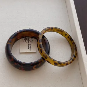 Close-up of leopard resin bangle set featuring a wide and narrow band in deep amber tones