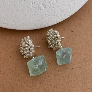 Detailed macro view of beaded silver studs with natural green gemstone drop pendants