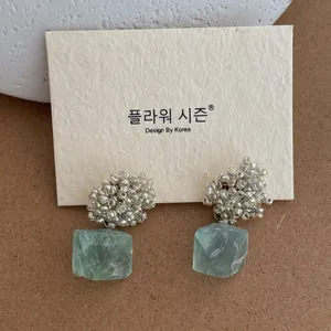 Detail of beaded stud earrings with irregular translucent light green stone pendants
