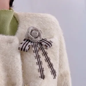 Spilla a rosa in tessuto grigio con fiocco a righe su cappotto color crema