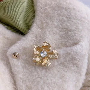 Spilla fiore dorata elegante con diamante centrale sul bavero di un cappotto bianco