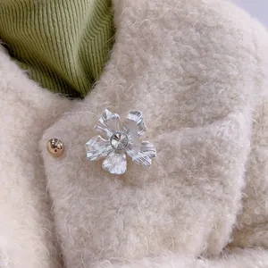 Dettaglio di una spilla a fiore argento con cristallo su un colletto di lana color crema