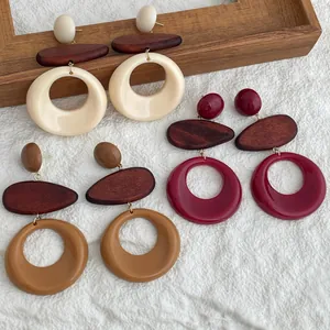 Detalle de pendientes geométricos de resina y madera en beige, granate y marrón caramelo