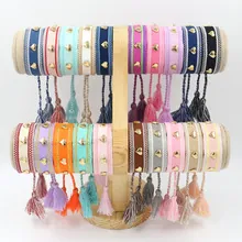 Detalle de pulseras tejidas de colores con dijes de corazón dorado y borlas en soporte de madera