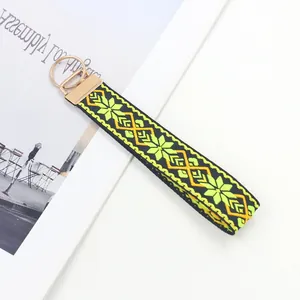 Detalle de un llavero de muñeca bordado bohemio con motivo floral amarillo y cierre de metal oro
