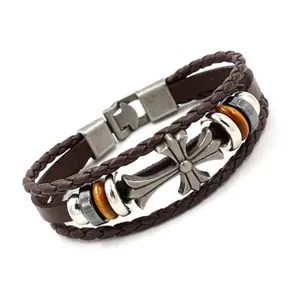 Dettaglio di un bracciale multistrato in pelle con croce argentata e cordino intrecciato