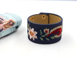 Détail d'un bracelet large en cuir PU bleu avec broderie florale et boutons-pression