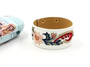 Gros plan d'une broderie paisley sur bracelet large en cuir blanc avec boutons pressions