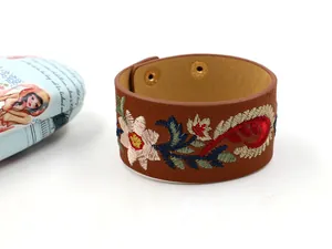 Détail macro du bracelet manchette en cuir marron avec broderie florale et boutons pression