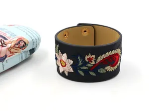 Détail macro de broderie florale sur bracelet en cuir large avec boutons-pression dorés