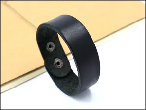 Dettaglio di un bracciale largo in pelle nera con texture e doppi bottoni a pressione