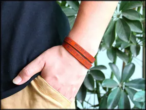 Close-up of brown leather wrap bracelet with embossed BELIEVE text on a person's wrist