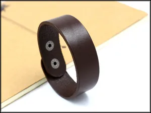 Dettaglio macro del bracciale largo in pelle marrone scuro con doppi bottoni automatici