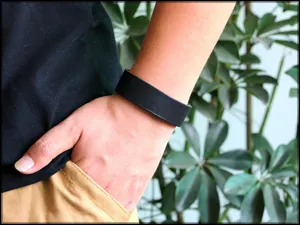Bracciale largo in pelle nera minimalista al polso con uno sfondo verde naturale