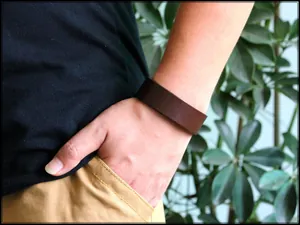 Primo piano di un ampio bracciale in pelle marrone indossato da un modello all'aperto