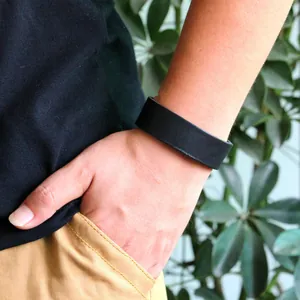 Bracciale largo in pelle nera minimalista per uomo e donna sul polso del modello con texture