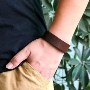 Bracciale largo in pelle marrone scuro minimalista indossato al polso in ambiente naturale